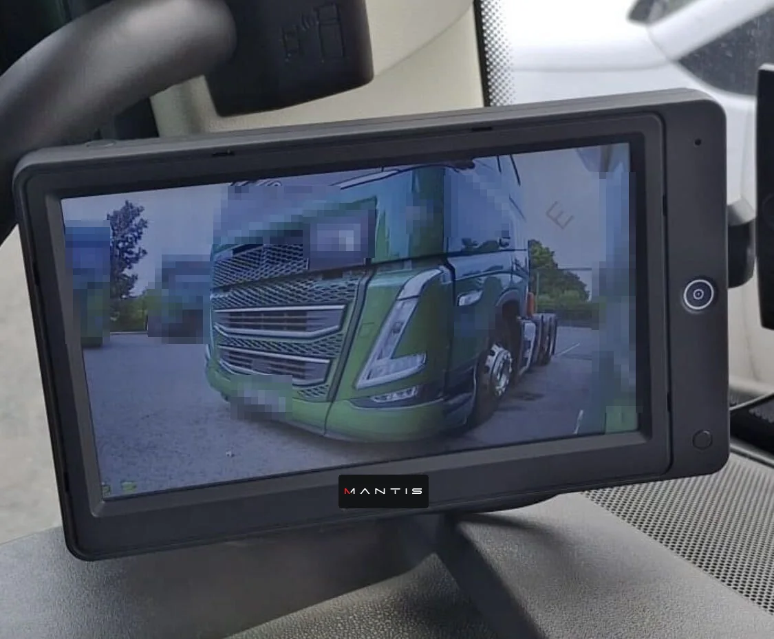 A MANTIS screen mounted at the A-pillar of a truck cab, showing a side-camera view of another truck in a yard