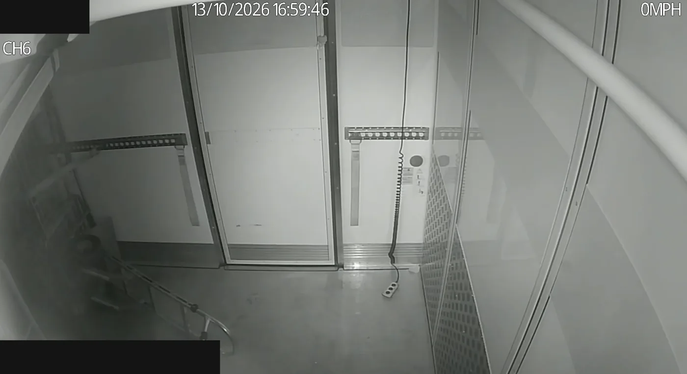 A grey night-time camera view inside a refrigerated body with the doors closed, the walls, straps and floor clearly visible