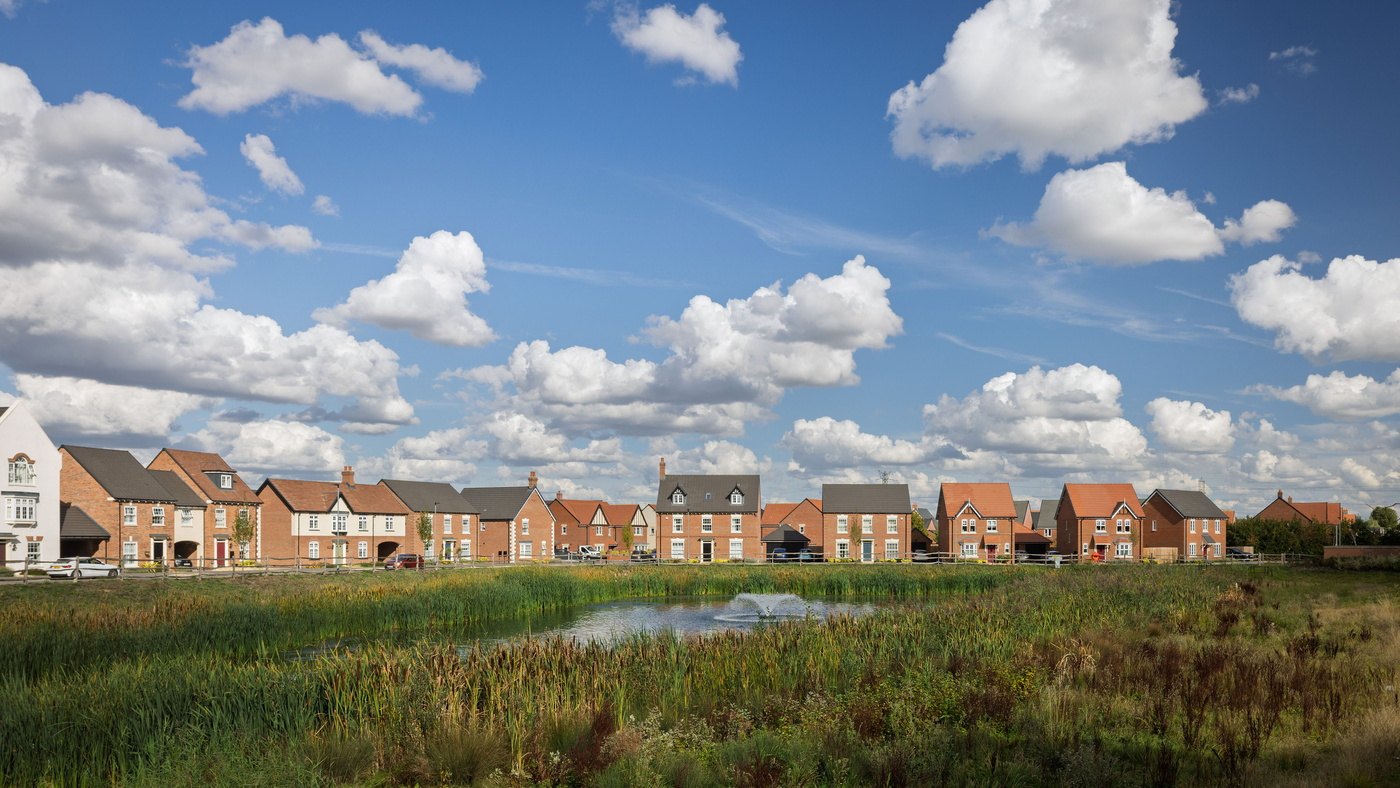 A completed Davidsons Homes development of brick houses seen across a landscaped balancing pond under a blue sky