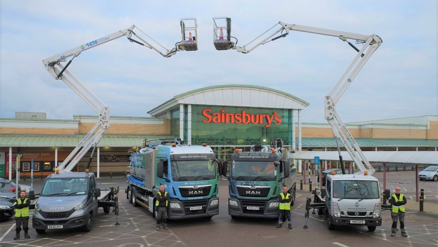 Four KSD Group service vehicles outside a supermarket, two with elevated platform booms raised, engineers in high-visibility clothing standing beside them