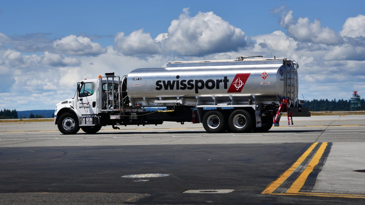 A Swissport aviation fuel tanker crossing an airport apron under a blue sky