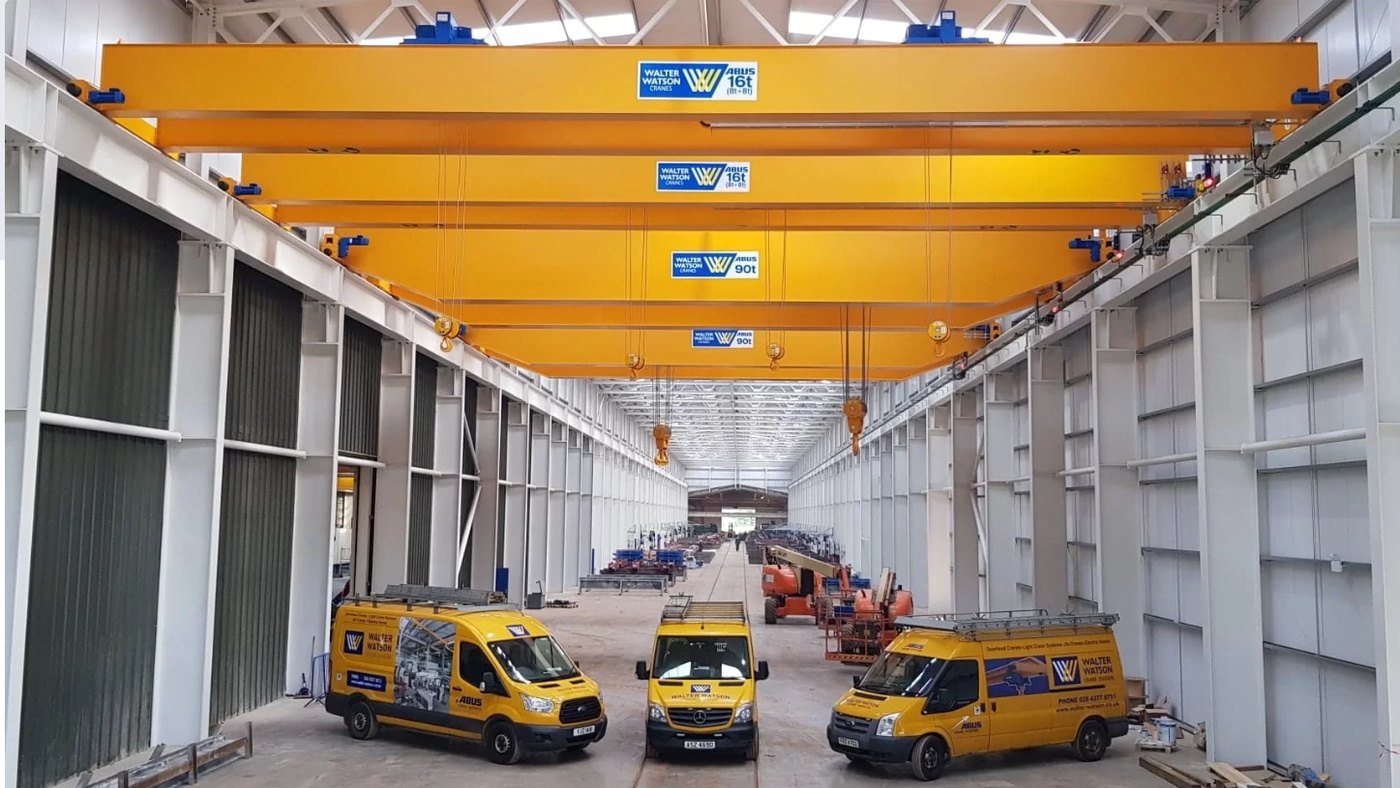 Three yellow Walter Watson service vans parked inside a large industrial hall beneath overhead travelling cranes carrying Walter Watson Cranes branding